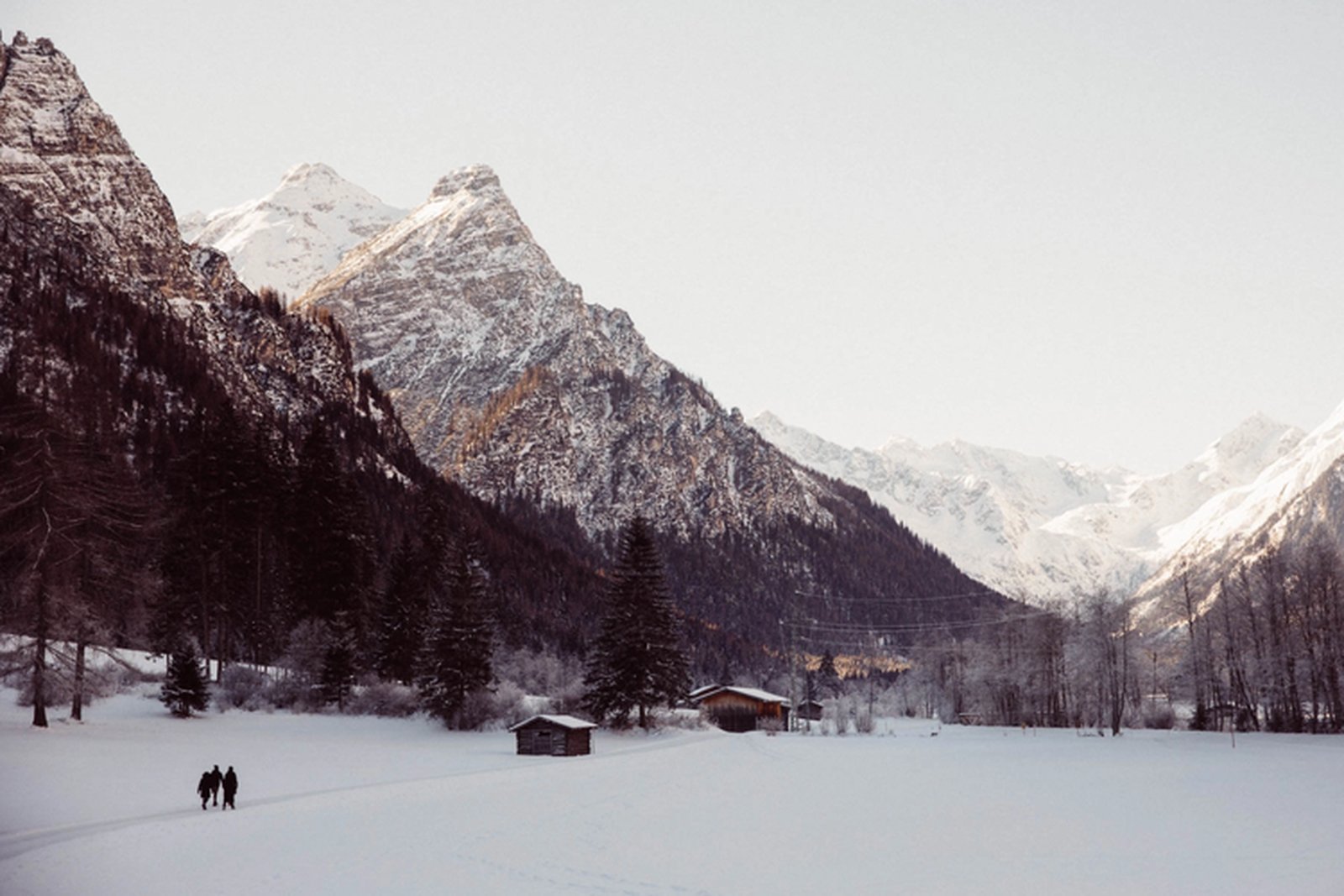 Wanderer gehen an einer Hütte unter den verschneiten Gipfeln des Gschnitztals vorbei