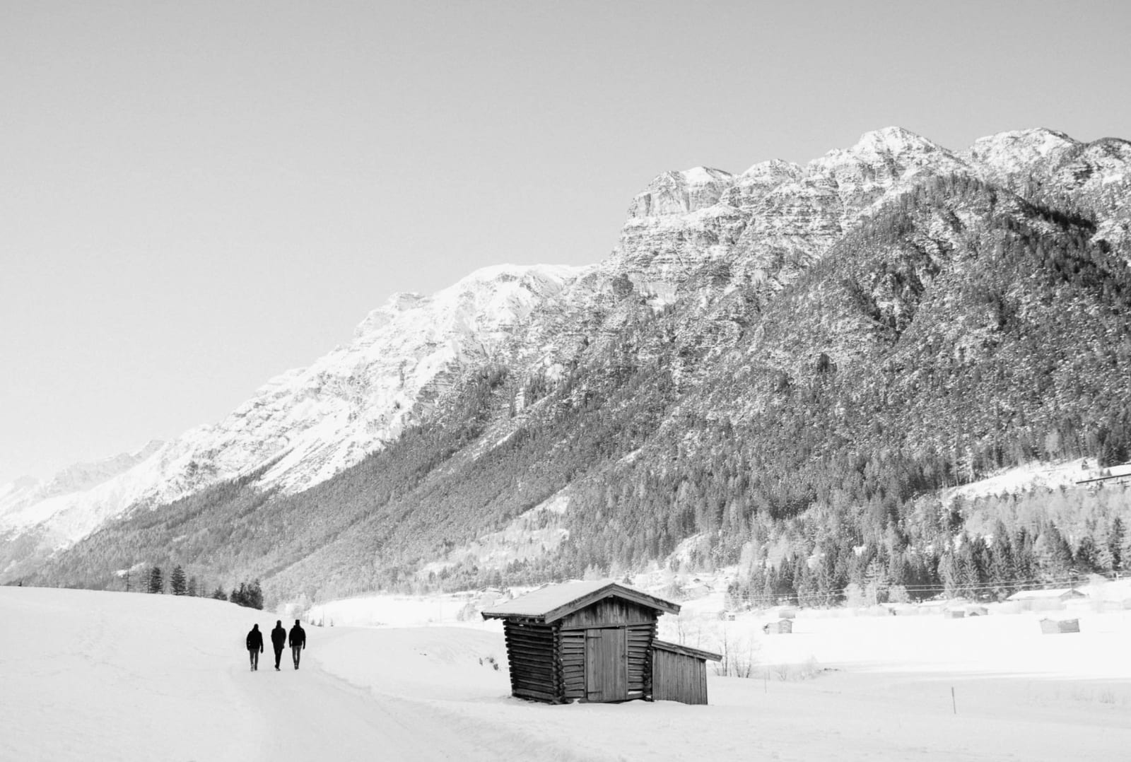 Wanderer gehen an einer Hütte unter den verschneiten Gipfeln des Gschnitztals vorbei